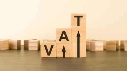 Vat on wooden cubes over yellow background with copy space, financial concept