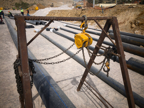 Manual Hoist And PVC Pipes In Protective Metal Covers. Industrial Pipeline Mantling At Construction Site