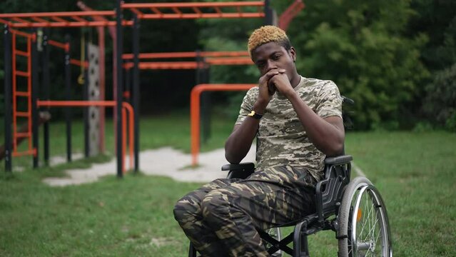 Devastated frustrated man in wheelchair sitting outdoors in park at sports ground thinking. Portrait of sad depressed African American ill guy on summer day outdoors. Live camera zoom in, slow motion