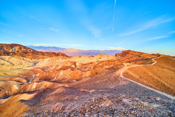 Wide view of hiking path along top of mountains at Death Valley with colorful sunrise waves
