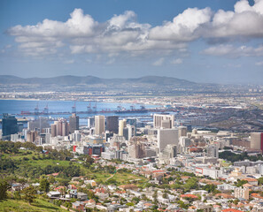 Fototapeta na wymiar Landscape of buildings in an urban town with greenery along the mountain and sea. Copy space with views from Signal Hill in Cape Town, South Africa of a cloudy blue sky over a beautiful coastal city