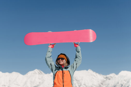Happy lady holding snowboard over head on mountain peak