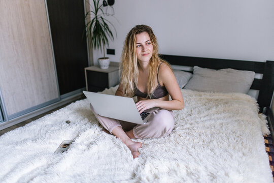 Female freelancer with laptop on legs resting in bedroom