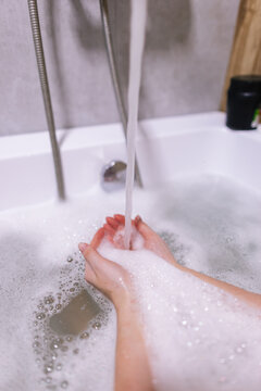 Person holding hands under water with lather, which pouring from tap