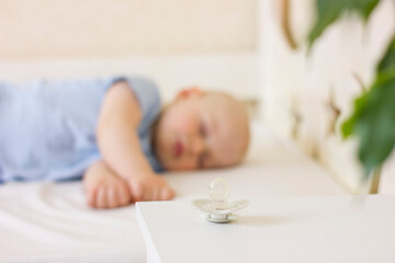 Obraz na płótnie Canvas Little baby boy is peacefully sleeping and a pacifier dummy liying on table near bed.
