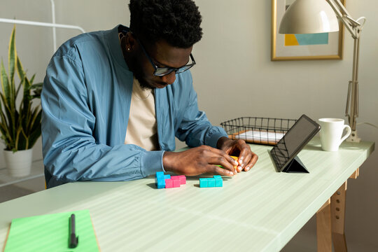 Black man making wooden geometric puzzle in office