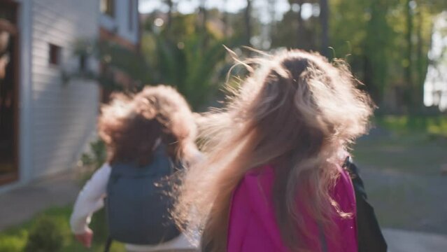 Two school girls run along street with fluttering curly hair on sunny day