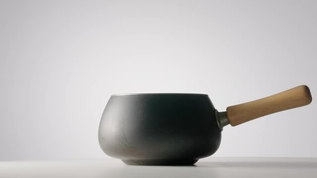 Gray cast iron frying pan or saucepan with wooden handle rotating on light gray isolated background. Stainless steel cooking pot. Saucepan, stewpan, kitchen utensils. Deep frying pan. Fondue.
