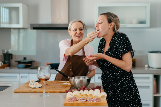 Mother giving snack to her adult daughter in kitchen while cooking