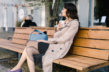 Beautiful woman in a coat enjoying a takeaway coffee on a bench