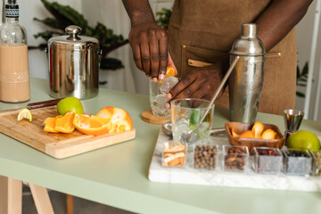 Cropped bartender squeezing orange in cocktail