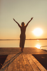 A girl in a long dress walks along a wooden bridge in the sunset
