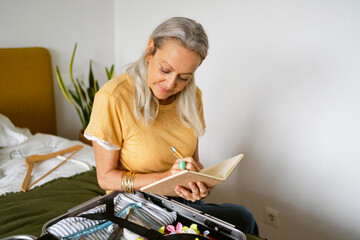 Gray-haired woman checking list by travel luggage