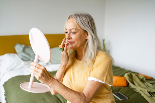 White hair Mature female painting holding hand mirror by bed