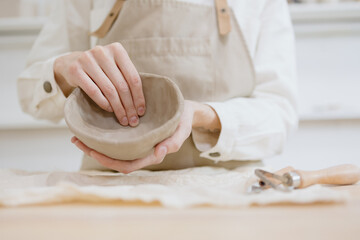 woman ceramist in the workshop makes mugs out of clay. a small business or hobby is the creation of ceramic products. an oriental young woman ceramist makes dishes and vases out of clay. handmade