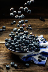 Fresh blueberries in an enamel bowl on a wooden rustic table, close up view. Levitating blueberries