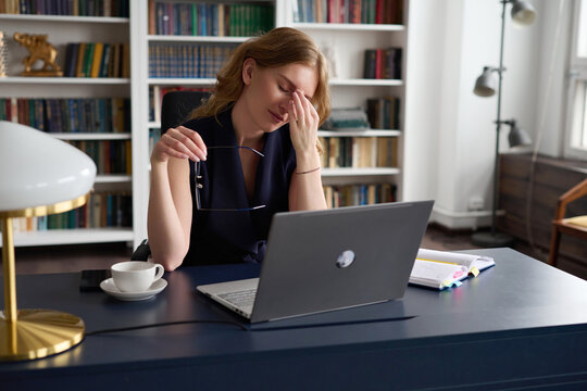 Overworked woman having migraine at table with laptop