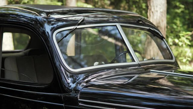 A close-up view of a black retro car in a summer green forest. Front view of the black retro car.