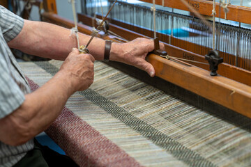 master craftsman working on a traditional wooden loom and hand weaving woollen herringbone cloth