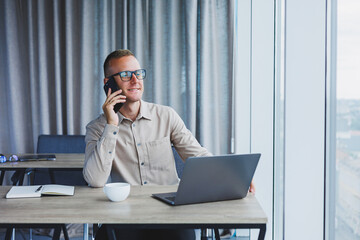 Successful man talking on smartphone and browsing netbook while surfing internet in office at table