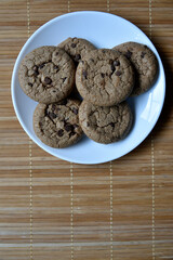Delicious oatmeal cookies with chocolate chips on a white plate on a mat. Sweet oatmeal cookies close-up.