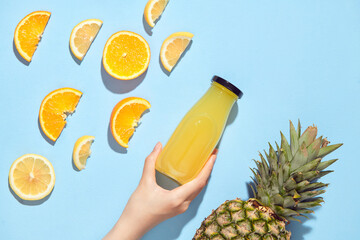 Hand holding bottle with fruit juice near pineapples slices