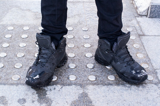 feet in black boots stand on an iron anti-slip coating in winter