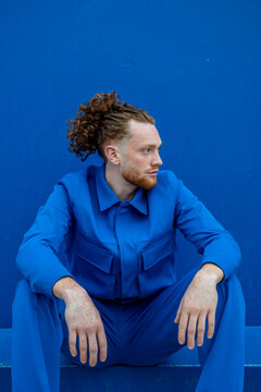 Man with ponytail resting against blue wall