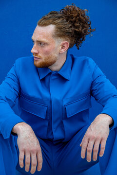 Man with ponytail resting against blue wall