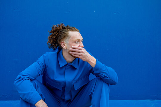 Man with ponytail resting against blue wall