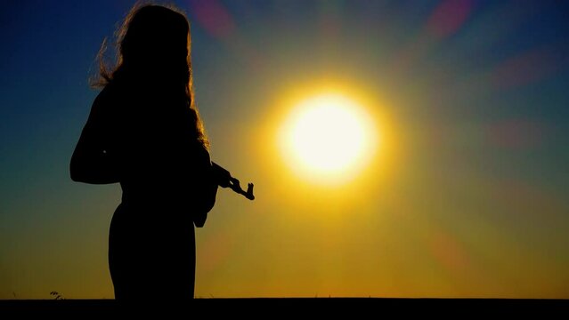 The problem of sexism. A young boy-girl with a Kalashnikov assault rifle at sunset. A transgender man with a Kalashnikov in a field at dawn. The concept of justice, equality, sexual minorities, LGBT.
