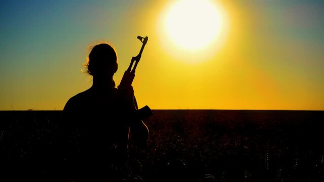 Ukraine War. A young man with a Kalashnikov assault rifle trains in the field. Silhouette of a man with a Kalashnikov assault rifle. The concept of war, terrorism, aggression against Ukraine.