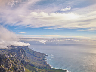 Aerial view of a calm ocean and mountains with a blue cloudy sky background and copy space. Stunning nature landscape of the sea and horizon from Table Mountain tourism destination in Cape Town