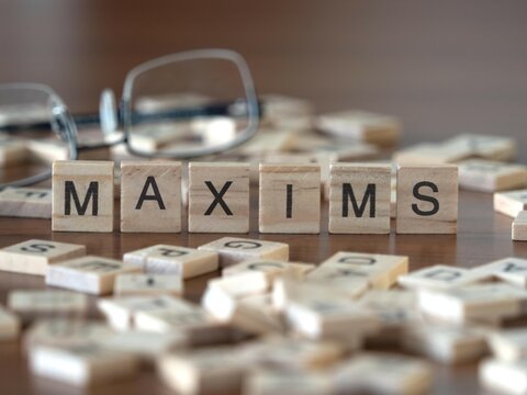 maxims word or concept represented by wooden letter tiles on a wooden table with glasses and a book