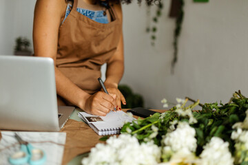 Cropped florist writing on notebook in studio