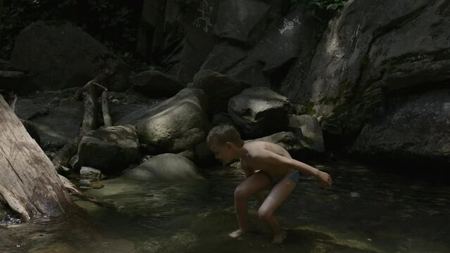A child on a journey. Creative. A little boy in underpants playing in the water and large rocks from the cliff are visible from behind.