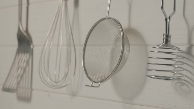 Spatula, whisk, masher and strainer hanging against rustic wooden white wall in restaurant or home kitchen. Kitchen utensils made of stainless steel or metal. Set of tools for cooking food.