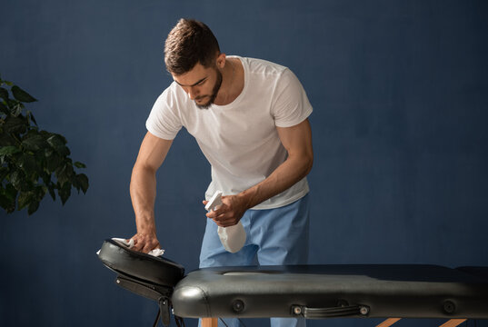 Masseur disinfecting massage table during work