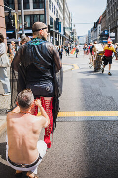 Man helps his buddy lace his red high heel boots during pride