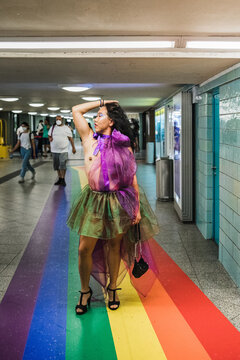 Asian man in rainbow coloured chiffon dress standing on rainbow floor