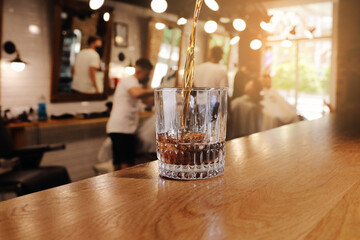 Whiskey is poured into glass. Glass of whiskey or cognac on bar counter in barbershop. customers are served an alcoholic drink in beauty men's salon