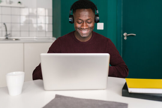 Cheerful black man listening to music and using laptop