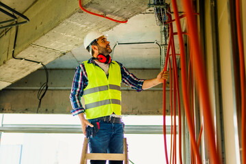 An experienced electrician who stands on a ladder and adjusts cable bellows for the electrical...