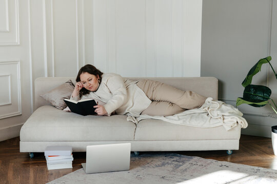 Young lady lying on couch and reading notes at home