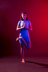 woman practices yoga  with neon light  on a colored background