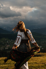 Ukrainian woman - hutsulka in the Carpathians  mountains in Ukraine from the back. In traditional national costume - embroidered shirt, vyshyvanka skirt, belt at sunset. Symbol of freedom. Verkhovyna