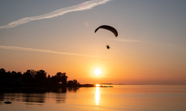 Paraglider pilot flies in the sky during sunset on beautiful beach. Paraplane silhouette. Adventure vacation and travel concept.