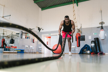 Dedicated black athlete exercising with battle ropes