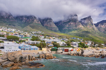 Fototapeta premium Landscape view of a seaside town along the mountain on a cloudy day in Cape Town, South Africa. Scenic view of a quiet and secluded residential area on the coast for tourists and holidays in summer