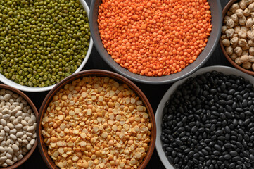 Overhead view of bowls of assorted raw legumes on a dark wooden table